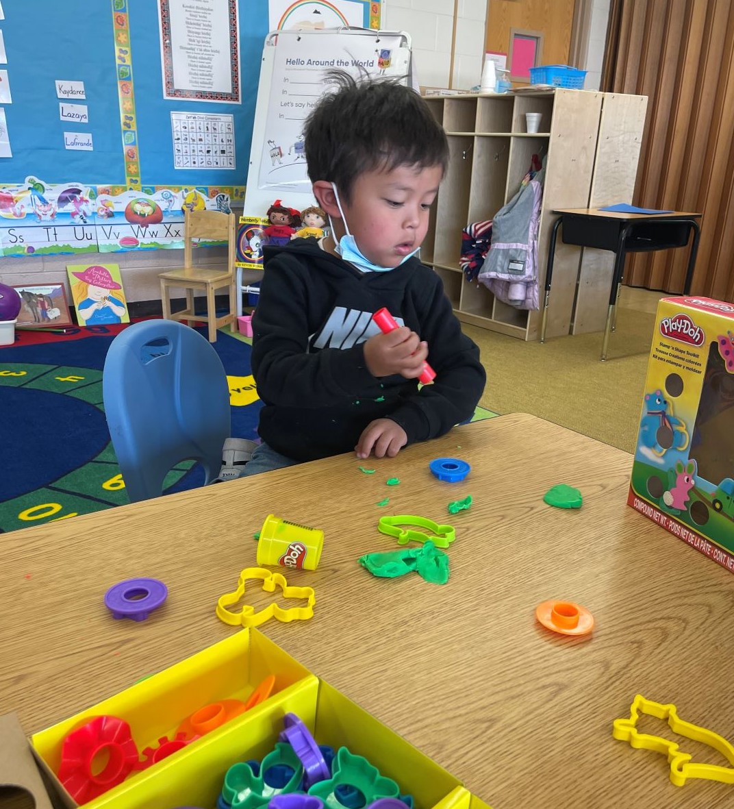 A young boy happily playing with various plastic toys in a vibrant classroom filled with educational materials.