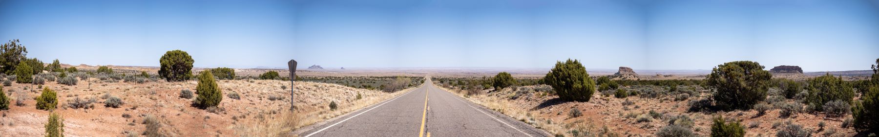 A scenic road lined with trees, leading to majestic mountains in the background under a clear blue sky.